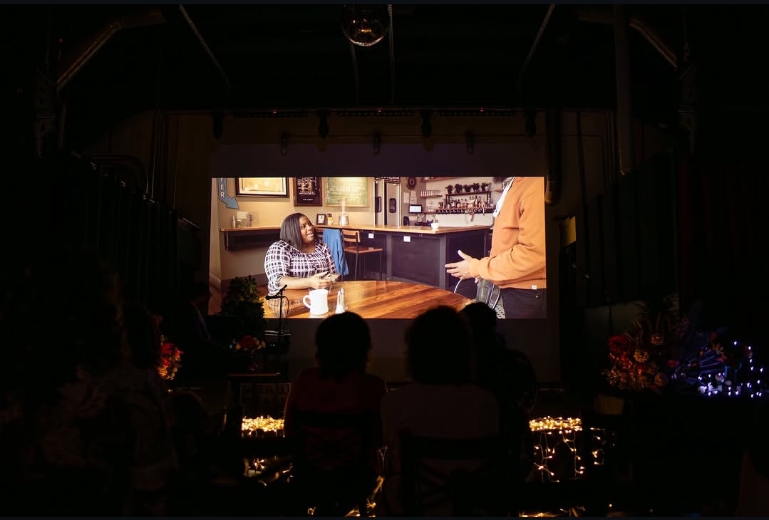 A film plays on the venue’s large screen as audience members watch together during Des Moines Art Week.