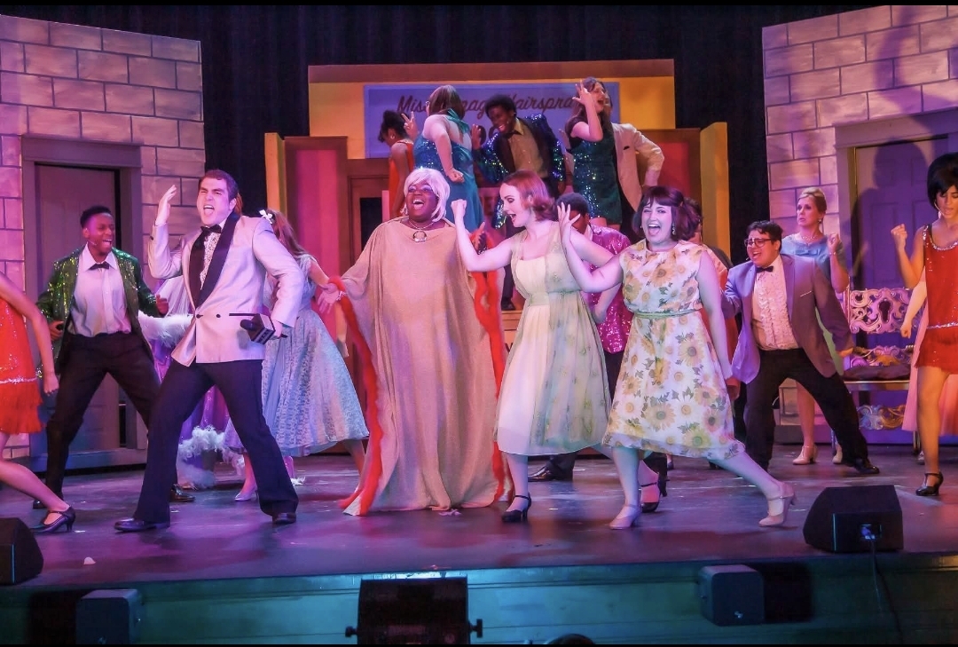 Colorful costumes and a full-stage musical number fill the scene with movement and personality. Every performer contributes to the energy of the moment.