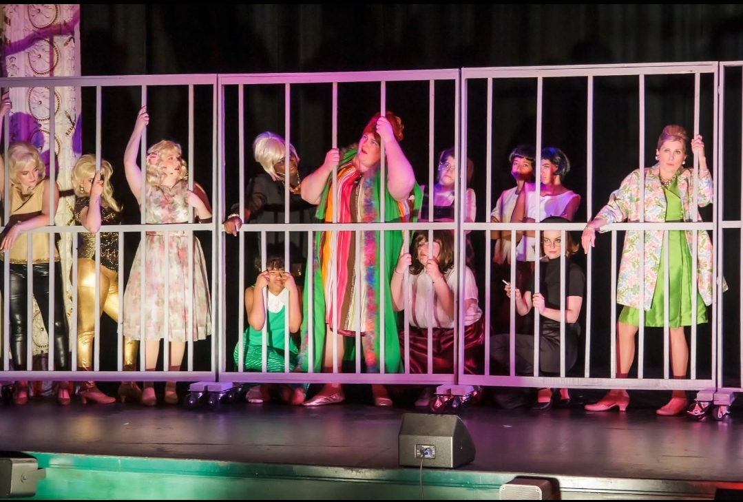 An ensemble scene staged behind bars brings character, humor, and expressive reactions into one frame, showing how a cast builds a story together.