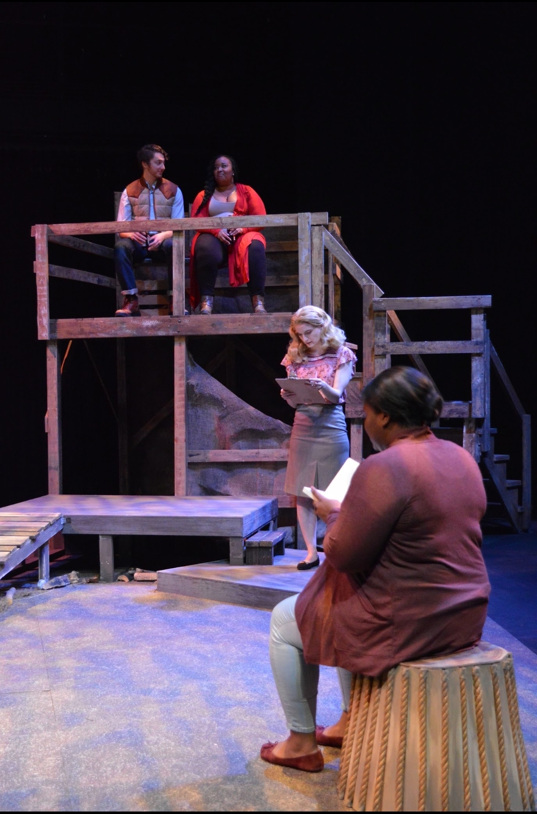 A scene unfolds across a wooden, multi-level set, with performers sharing the space and the audience’s attention. It reflects the timing and awareness that live storytelling requires.